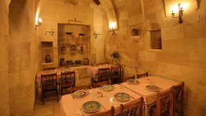 Comedor con paredes de piedra, mesas y sillas de madera. Varias mesas dispuestas con platos y cubiertos.