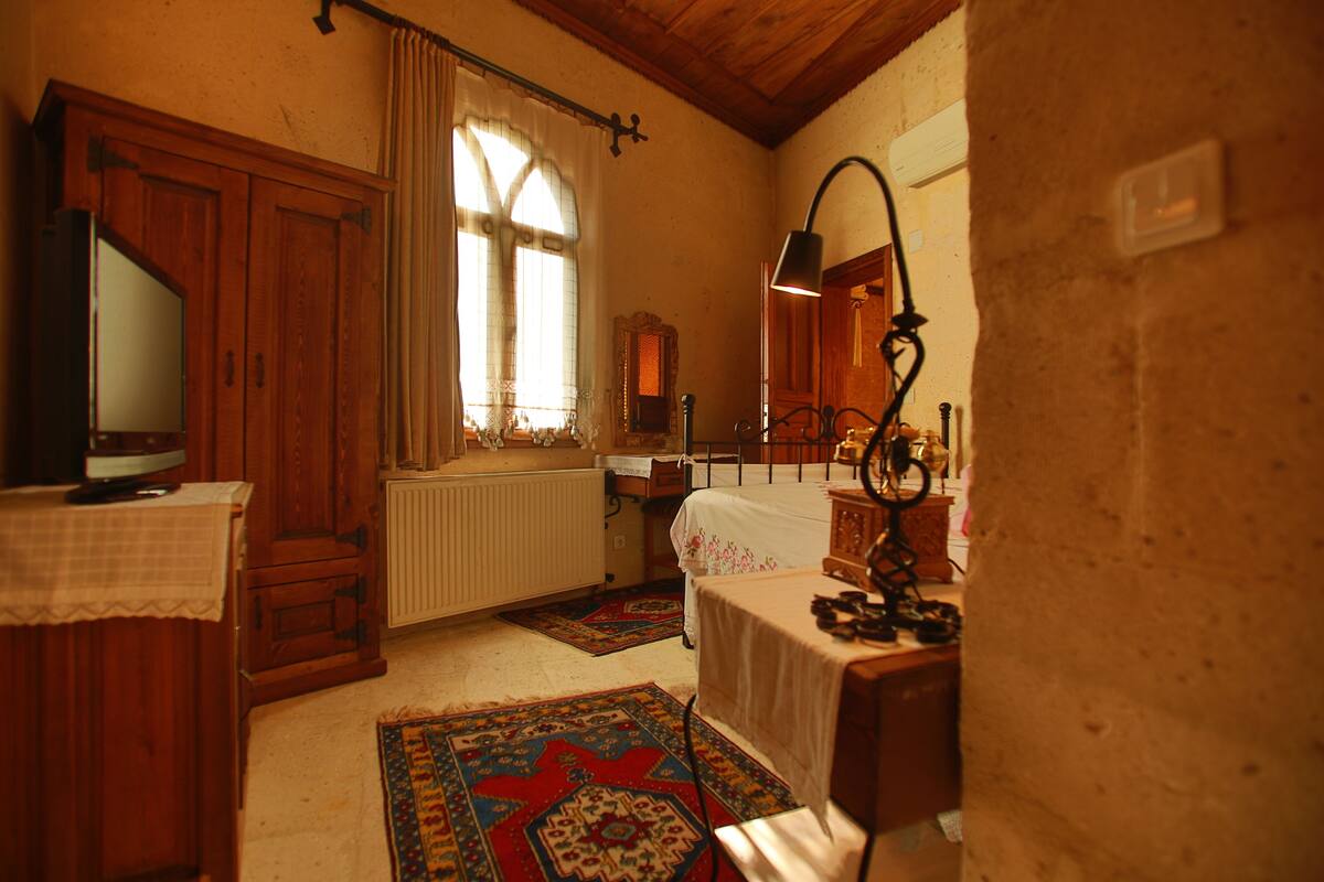 A traditional room with a wooden cabinet, a radiator, a bed with a patterned rug, and a desk with a lamp.