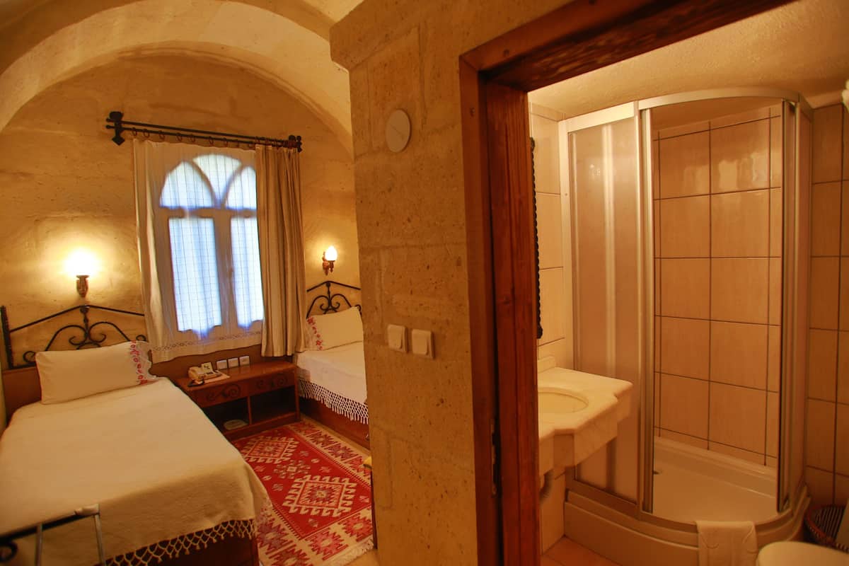 A bedroom with two beds, a window with curtains, a bedside table, and a red patterned rug.