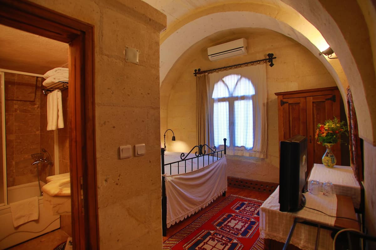 A bedroom with a bed, a bedside table with a vase, a window with curtains, and an arched ceiling.