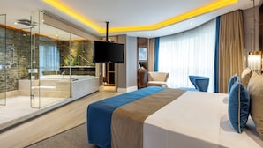 A modern hotel room with a large bed, a TV, a glass-enclosed shower area, and a view of the city. - AHC Old City Hotel (Istanbul)
