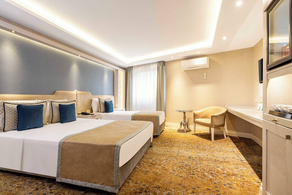 Habitación de hotel con dos camas, un escritorio, una silla y un televisor.