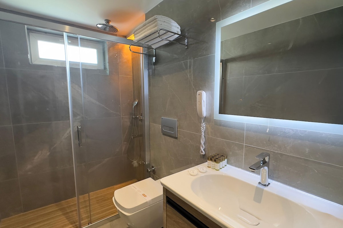 A modern bathroom with a glass-enclosed shower, a large mirror, a white sink, and a toilet.