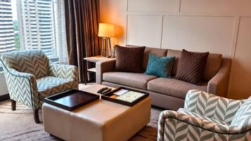 Une chambre d’hôtel avec un canapé, deux fauteuils, une table basse, une lampe et une vue sur la ville.