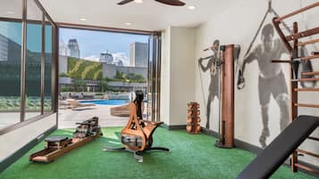 Enjoy a view of the pool from this room's large window, featuring a ceiling fan, rowing machine, pull-up bar, and bench.