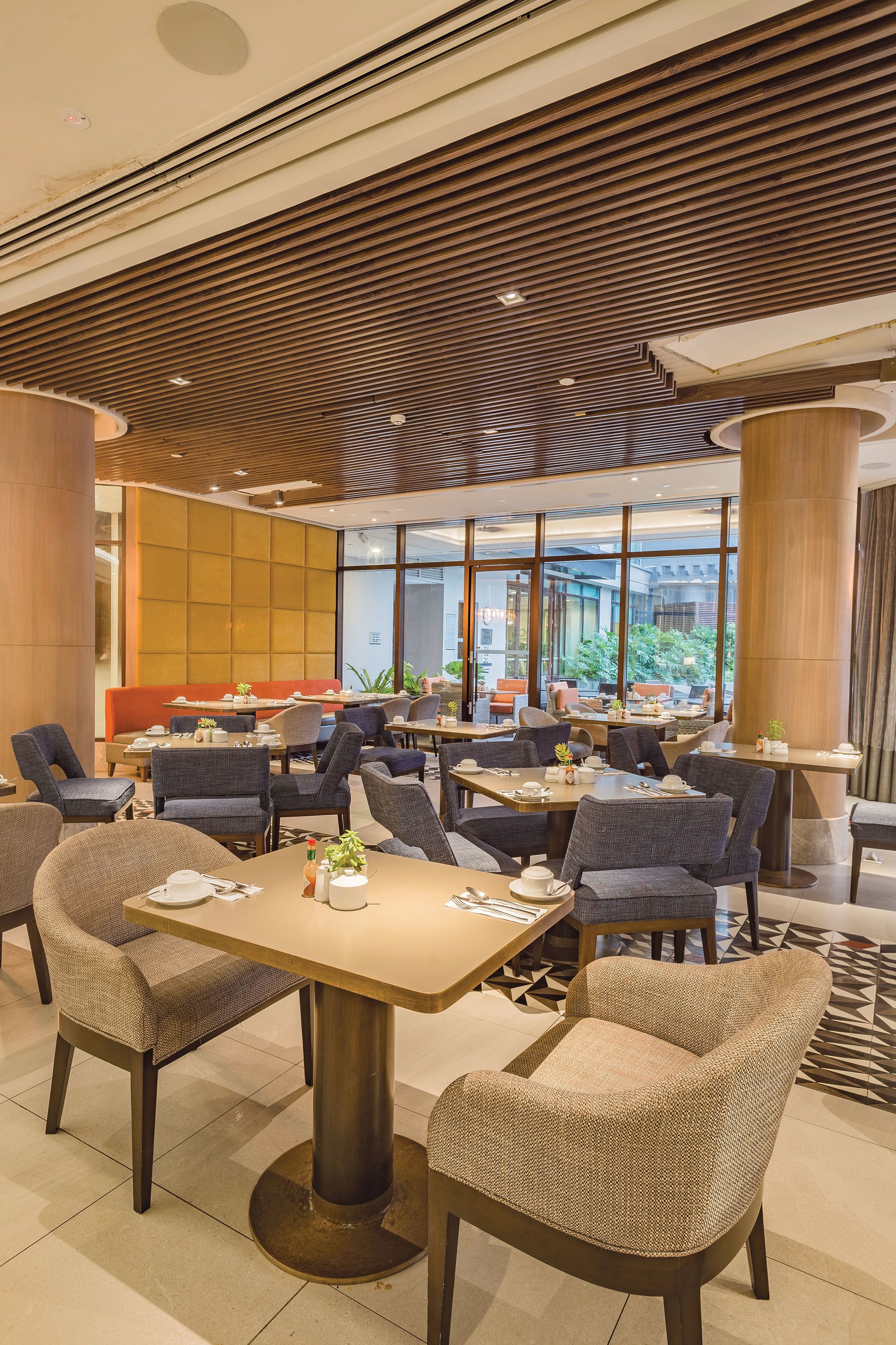 A modern dining area with multiple tables and chairs, large windows, and a wooden ceiling design.
