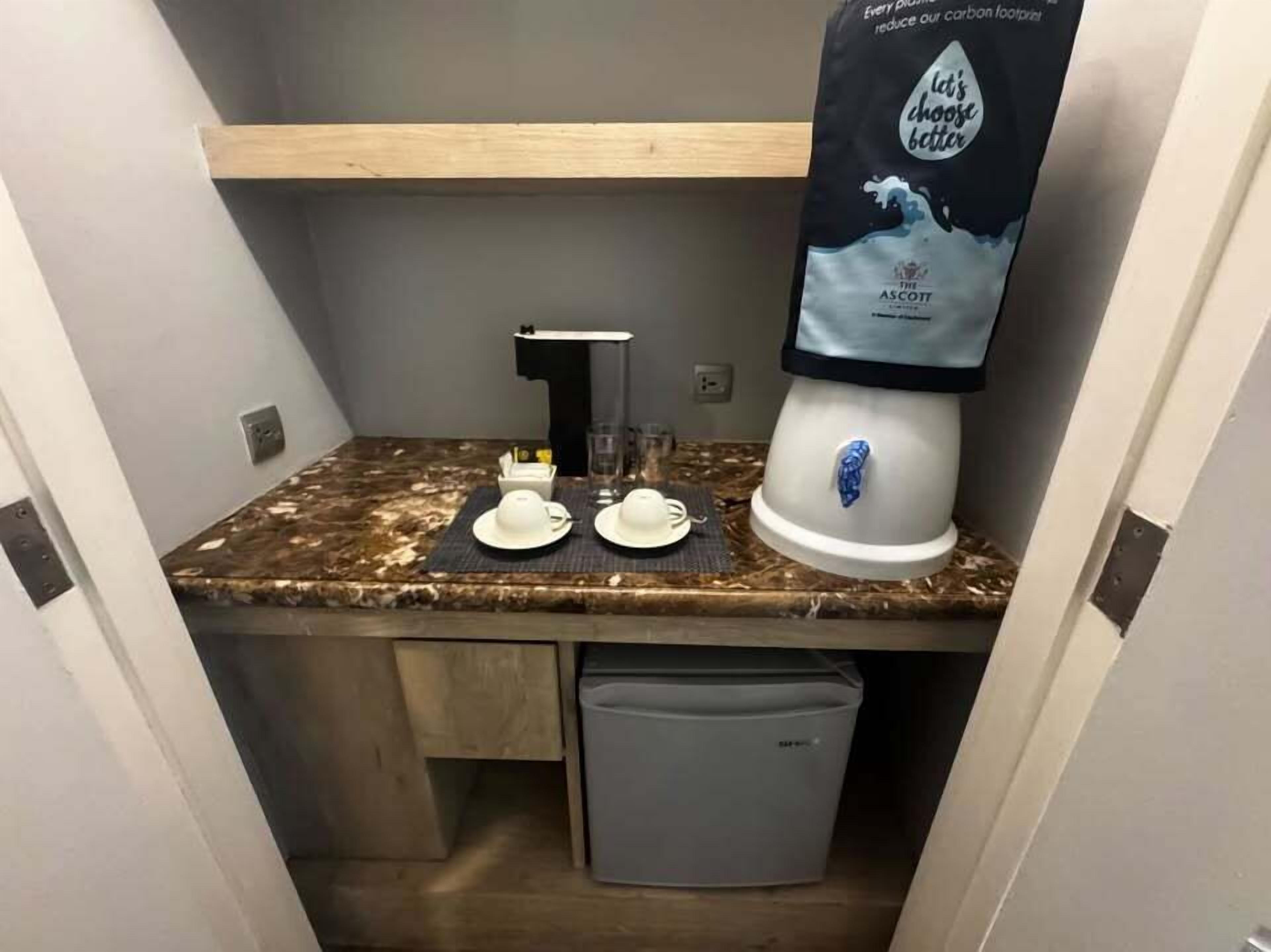 Una kitchenette compacta con cafetera, un lavamanos y un cubo de basura.