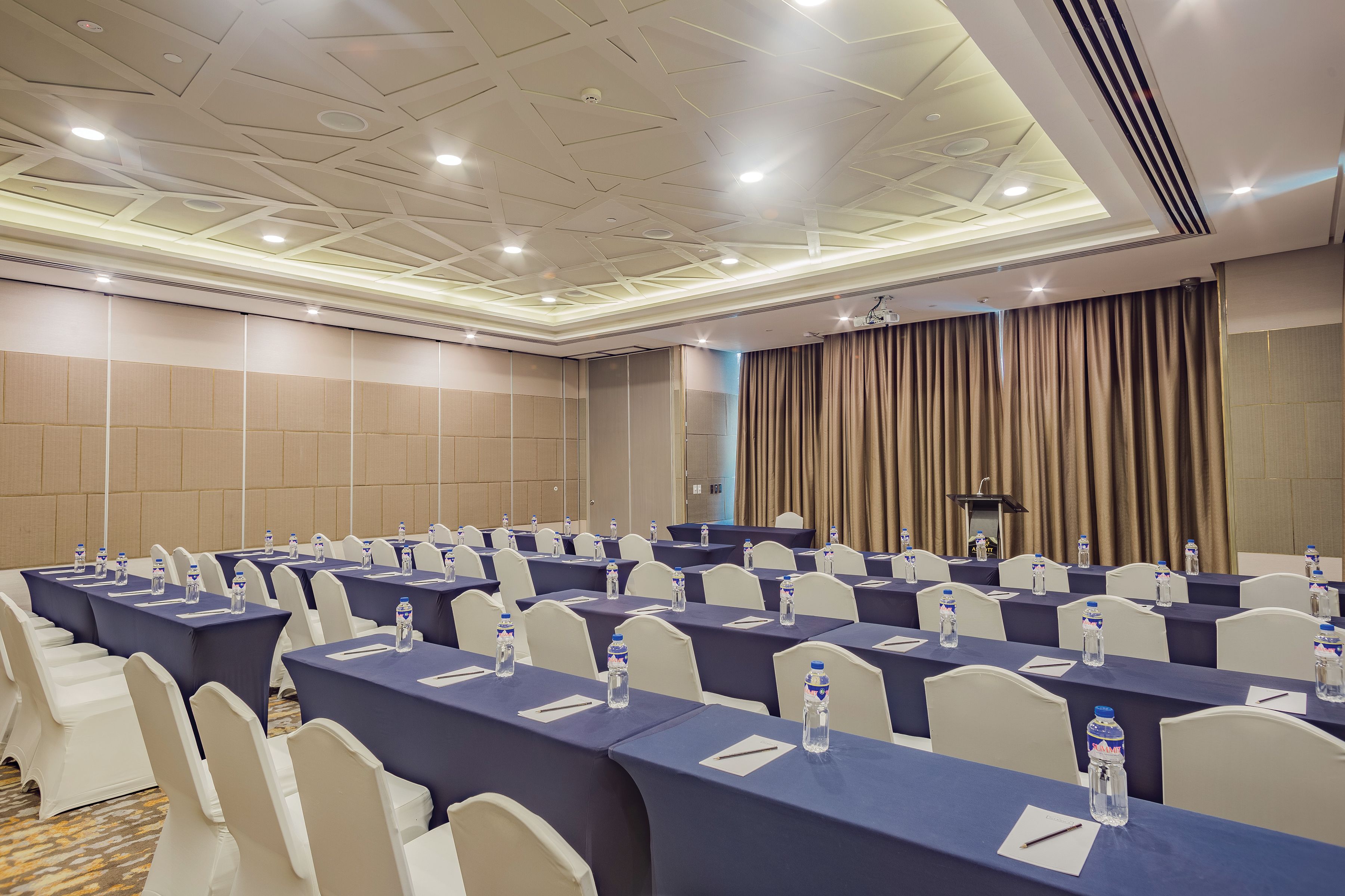 Un salón de conferencias con mesas, sillas y botellas de agua.