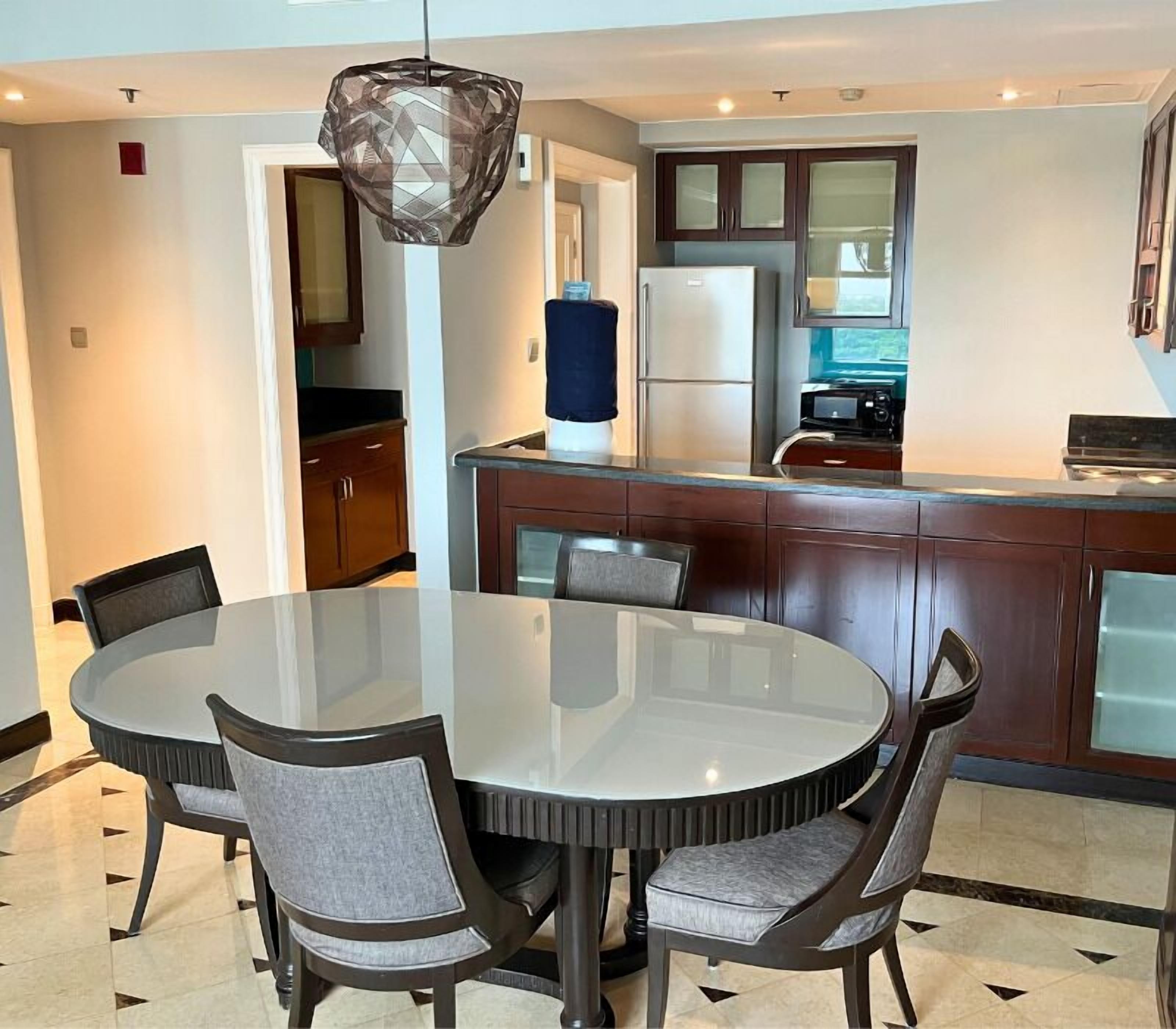 A modern kitchen with dark wooden cabinets, a round glass dining table, and a hanging pendant light.