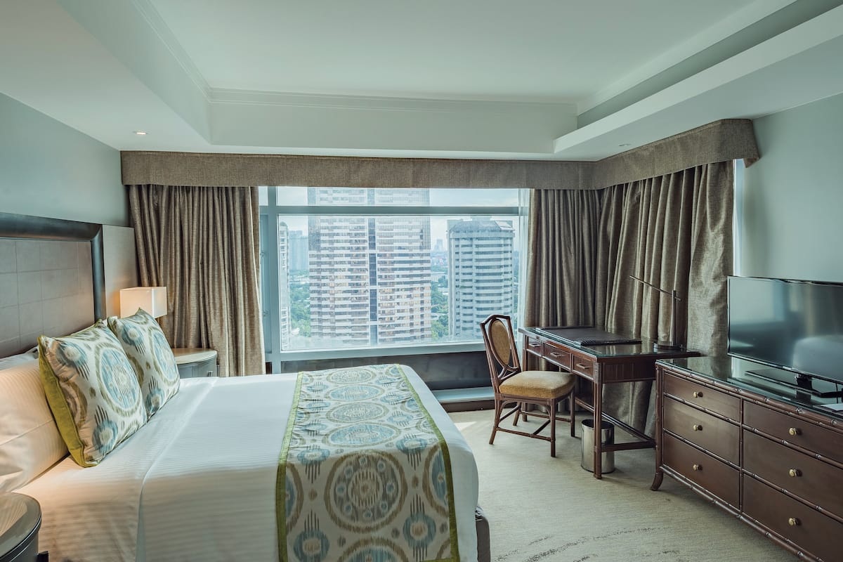 Una habitación de hotel con cama, escritorio, silla, televisor y un ventanal con cortinas.