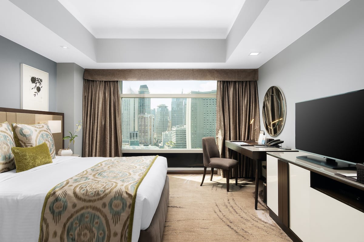 Habitación de hotel con una cama grande, un escritorio, una silla, un televisor y vistas a la ciudad.