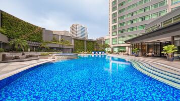 A swimming pool with a tiled blue floor, surrounded by lounge chairs and a building with a green wall.