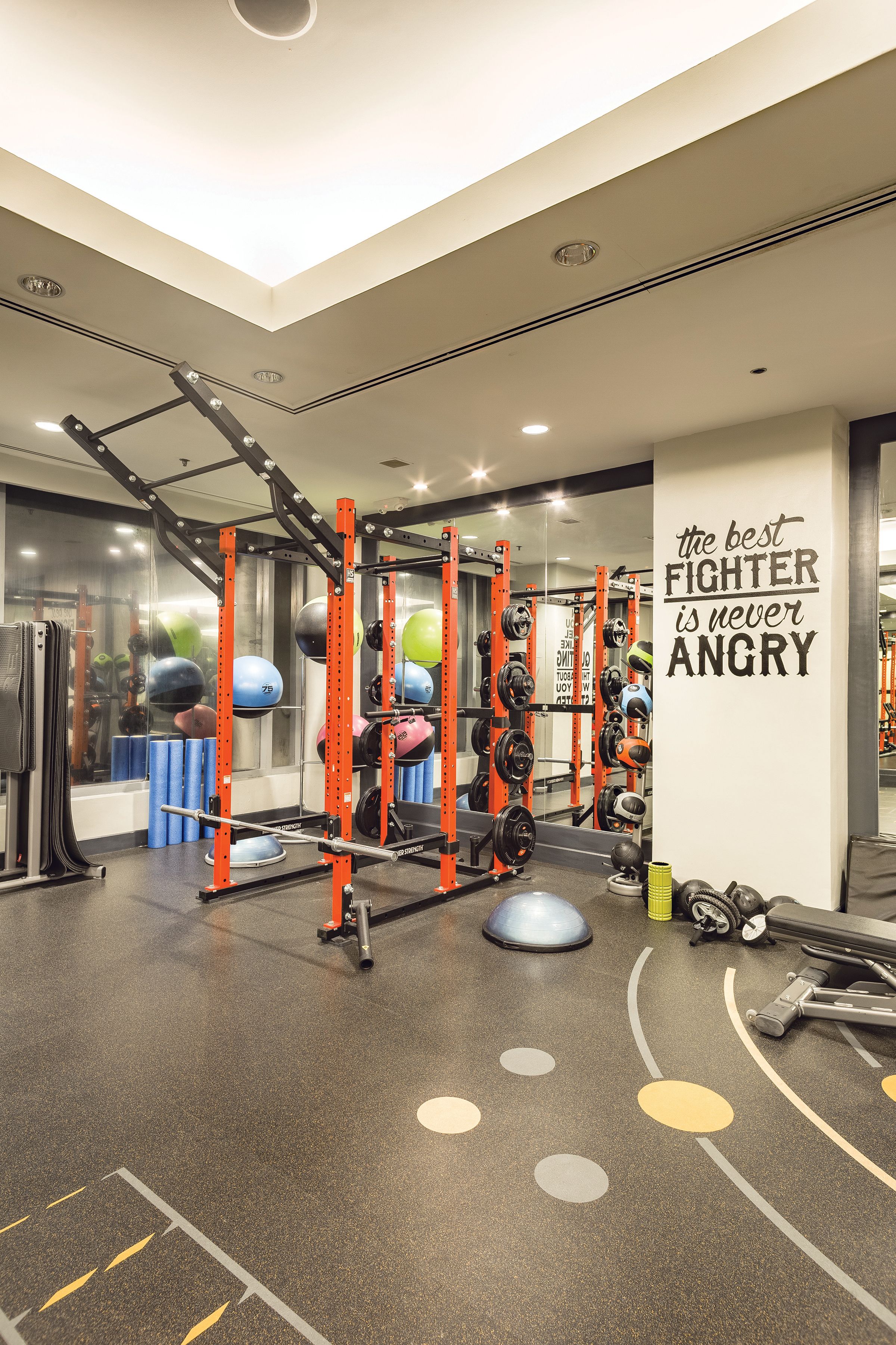 Ein Fitnessraum mit Krafttrainingsgeräten, einem motivierenden Spruch an der Wand und einem Spiegel, der die Geräte reflektiert.