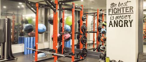 A gym with weightlifting equipment, a motivational quote on the wall, and a mirror reflecting the equipment.