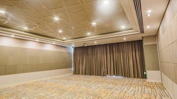 A conference room with a patterned carpet, a ceiling with recessed lighting, and a large curtain.