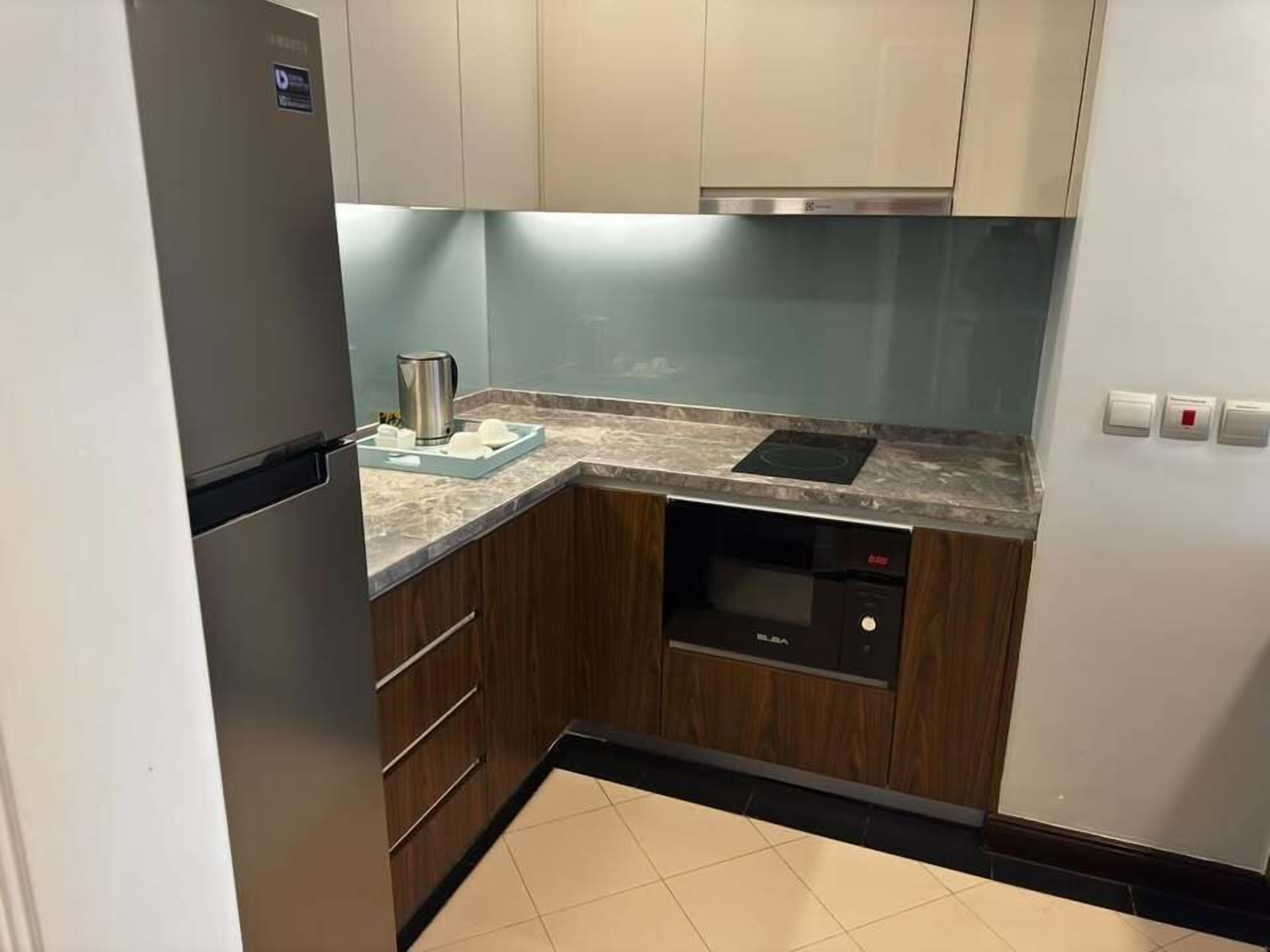 A compact kitchen with a built-in dishwasher, a stainless steel refrigerator, and wooden cabinets.