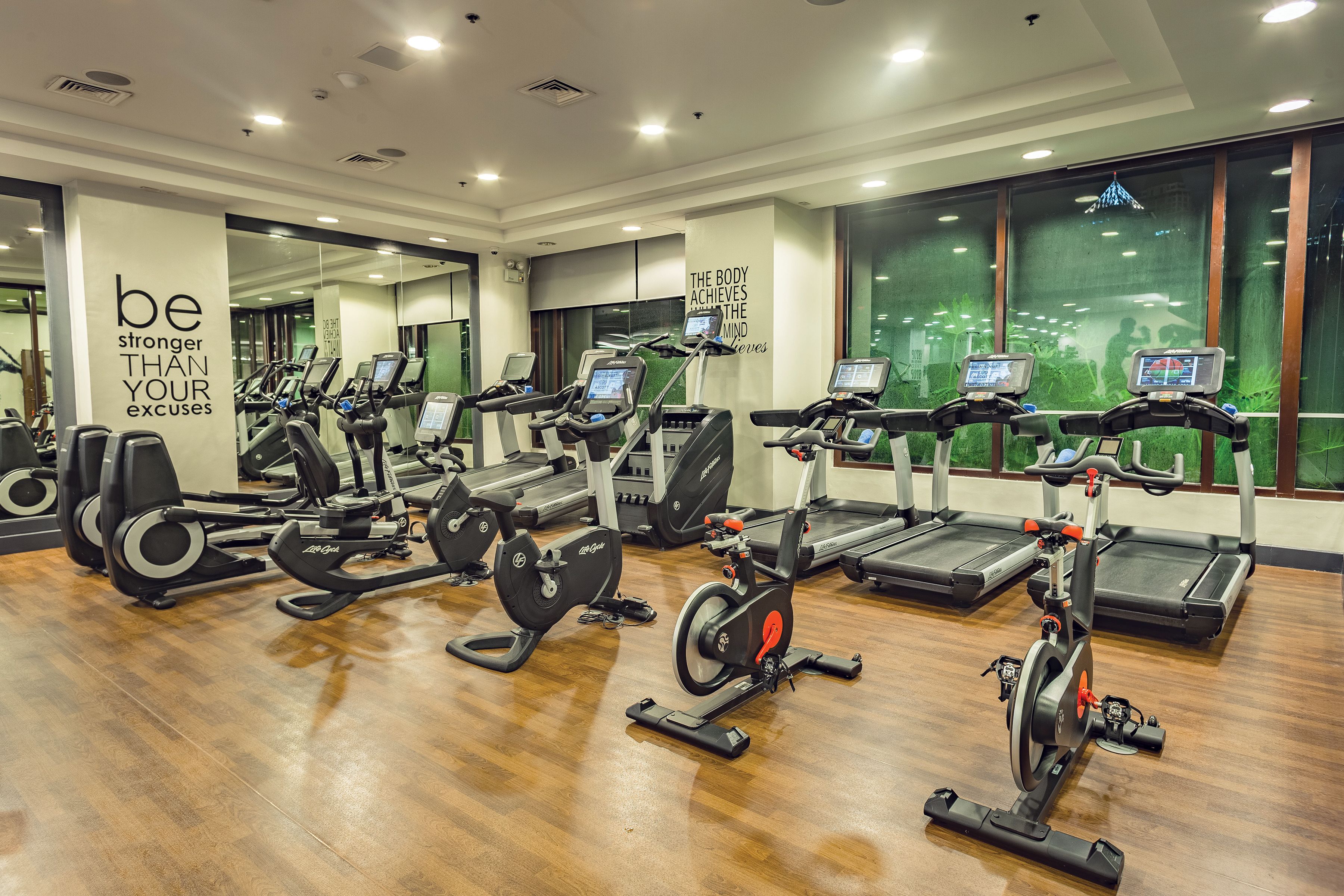 A gym with various cardio equipment, motivational wall text, and large windows.