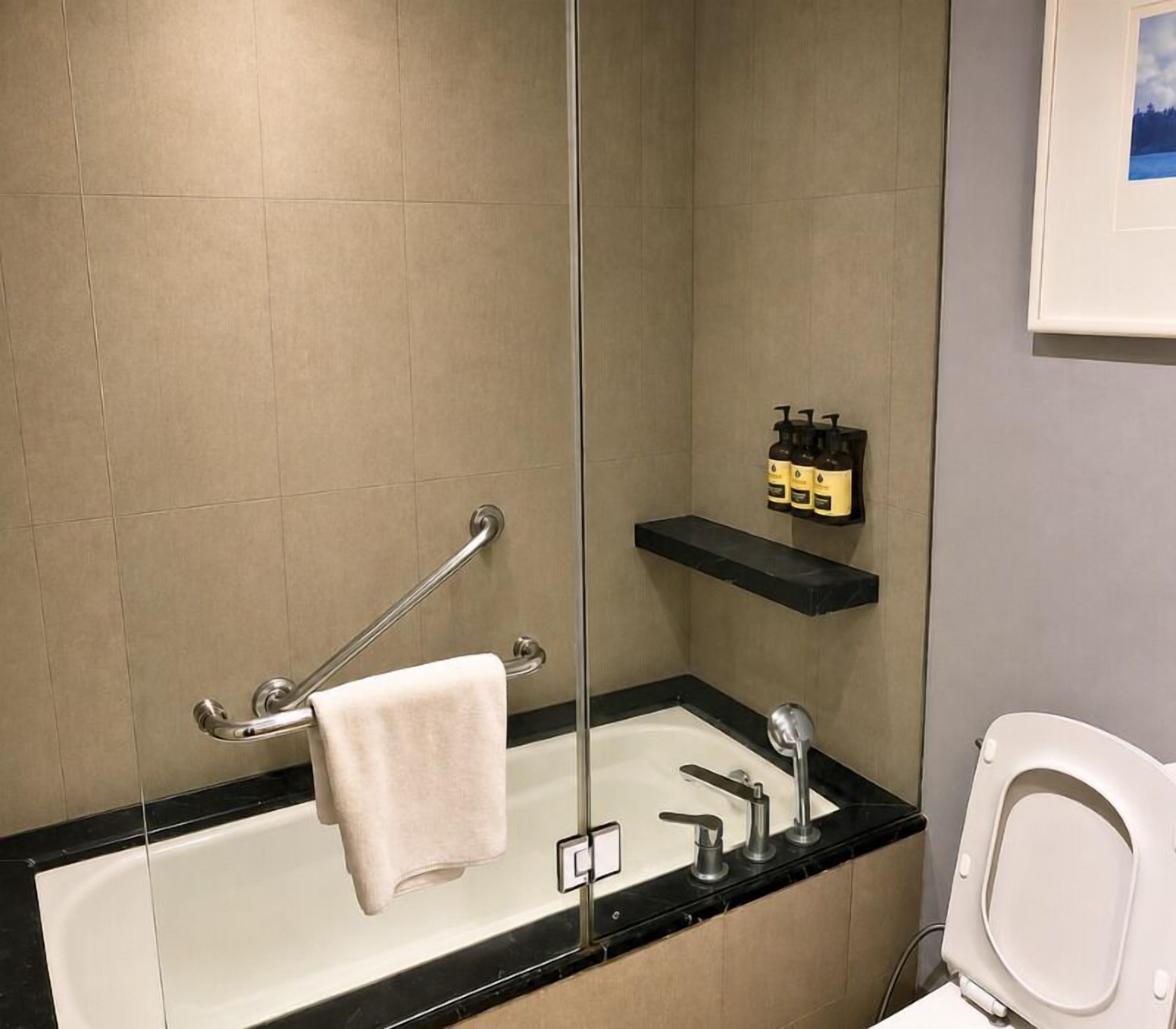 Ein Badezimmer mit einer Badewanne, einer Toilette, einem Handtuchhalter und einem Ablagebereich für Toilettenartikel.
