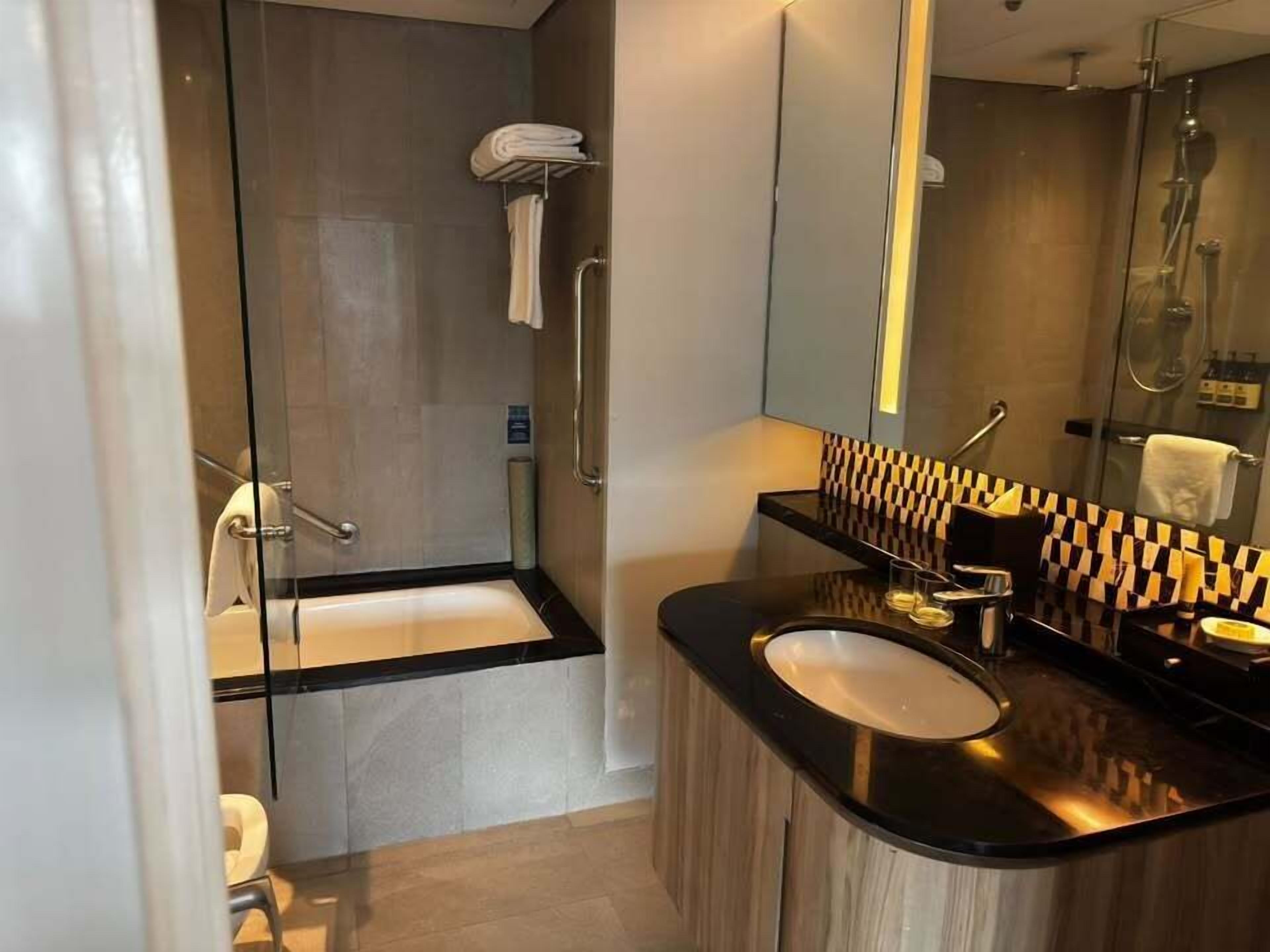 Un baño moderno con cabina de ducha de vidrio, lavamanos sobre encimera negra y espejo con resalte a cuadros.