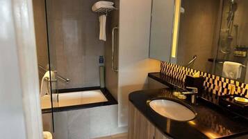 Un baño moderno con cabina de ducha de vidrio, lavamanos sobre encimera negra y espejo con resalte a cuadros.