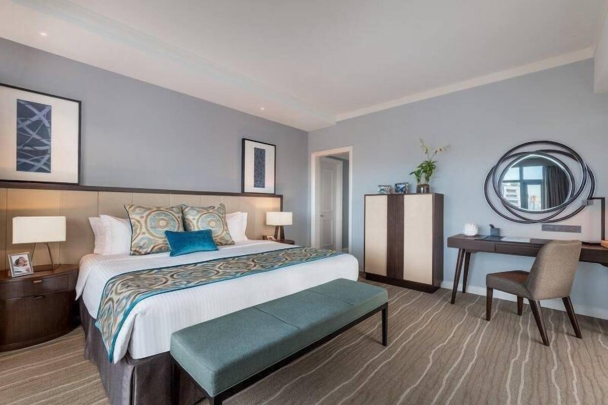 Habitación de hotel con cama, mesitas de noche, escritorio, silla, banco, armario y espejo.
