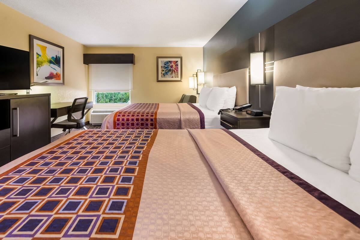 A hotel room with two beds, a desk, a TV, and artwork on the walls.