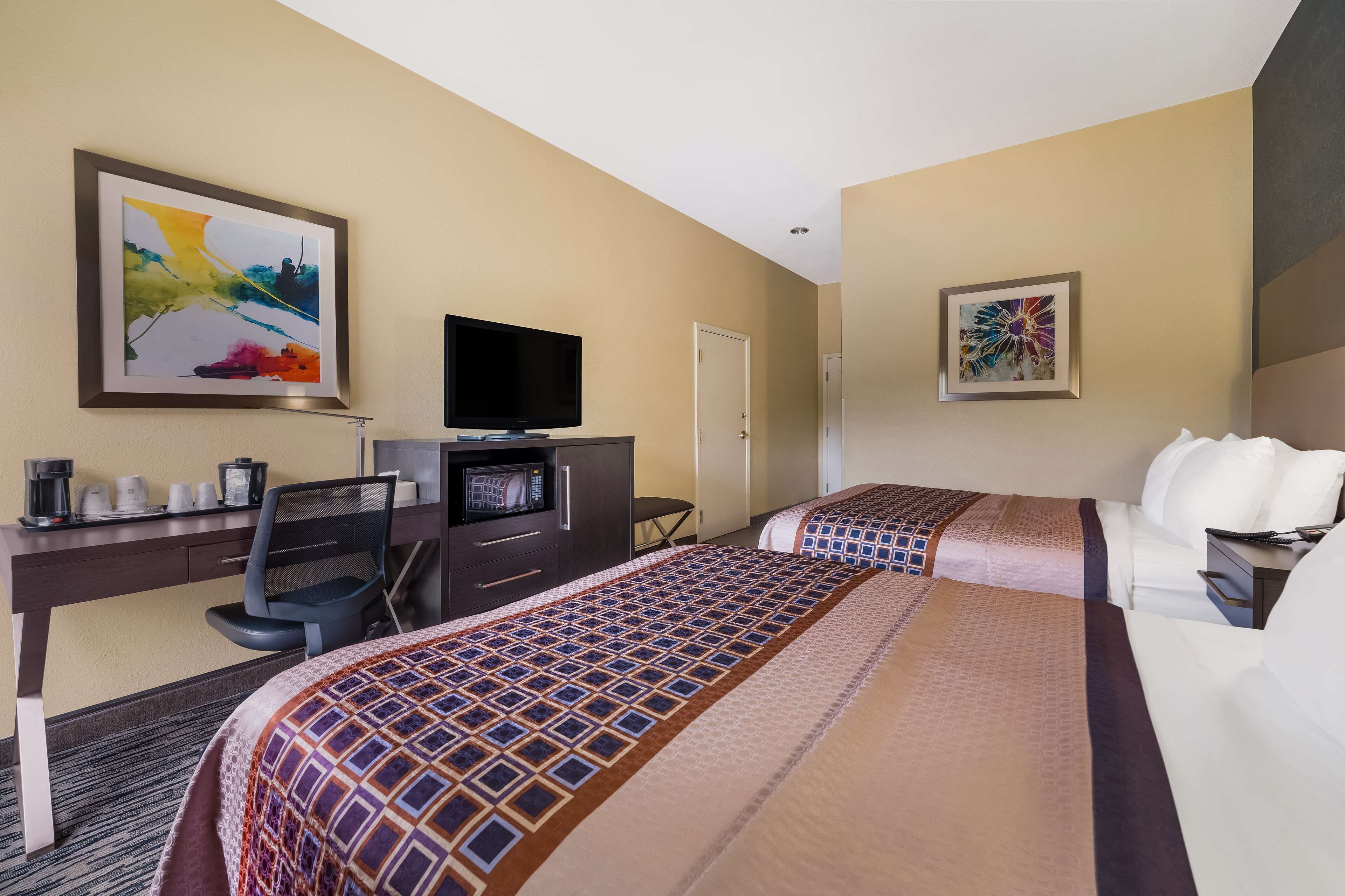 Habitación de hotel con dos camas, un escritorio, televisión, microondas y cafetera.