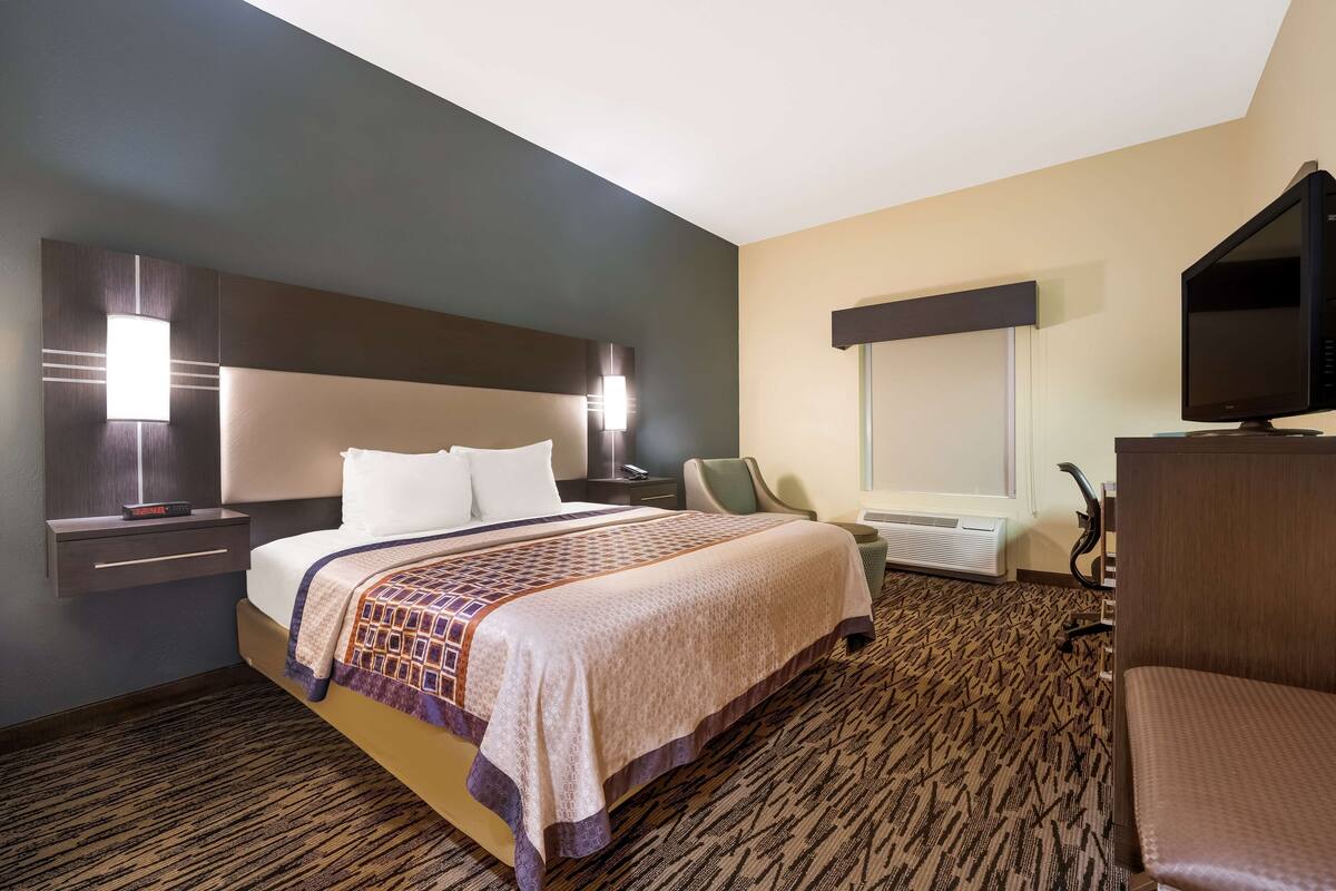 A hotel room with a large bed, a desk, a chair, a television, and a window.