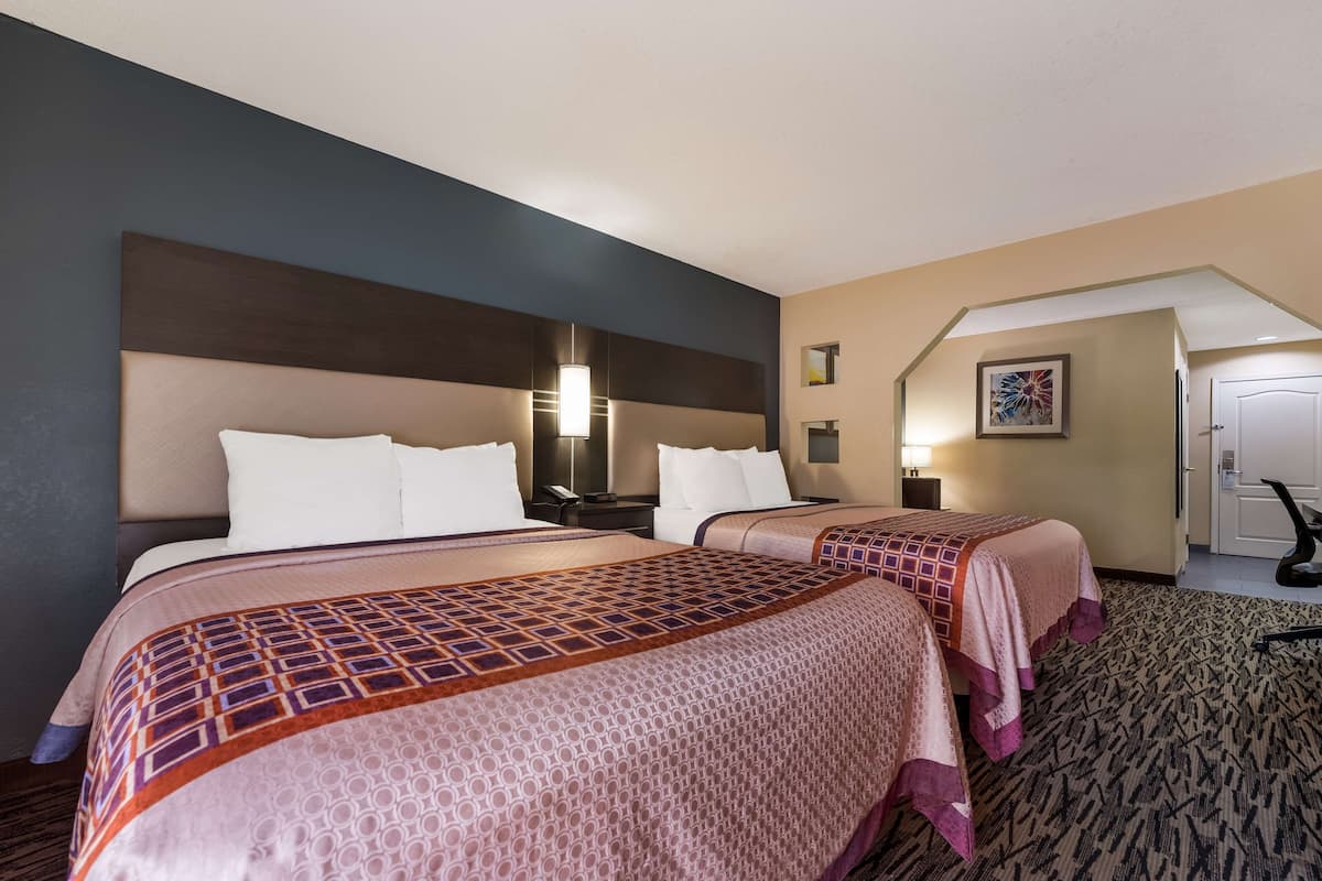 A hotel room with two beds, a headboard, a bedside table, a lamp, a framed picture, and a carpeted floor.