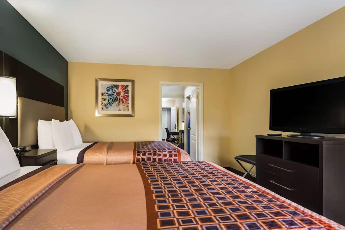 A hotel room with two beds, a TV, a desk, and a chair.