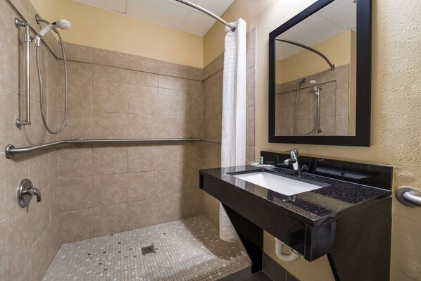 A bathroom with a shower, a handrail, a sink with a mirror, and tiled walls.