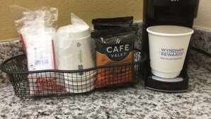 A coffee maker, a cup, and a basket with coffee bags and sugar packets. - Days Inn by Wyndham Athens, GA (Athens)