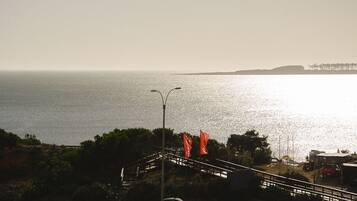 Une route côtière avec un pont menant à une plage, agrémentée de drapeaux orange et offrant une vue sur une côte lointaine.