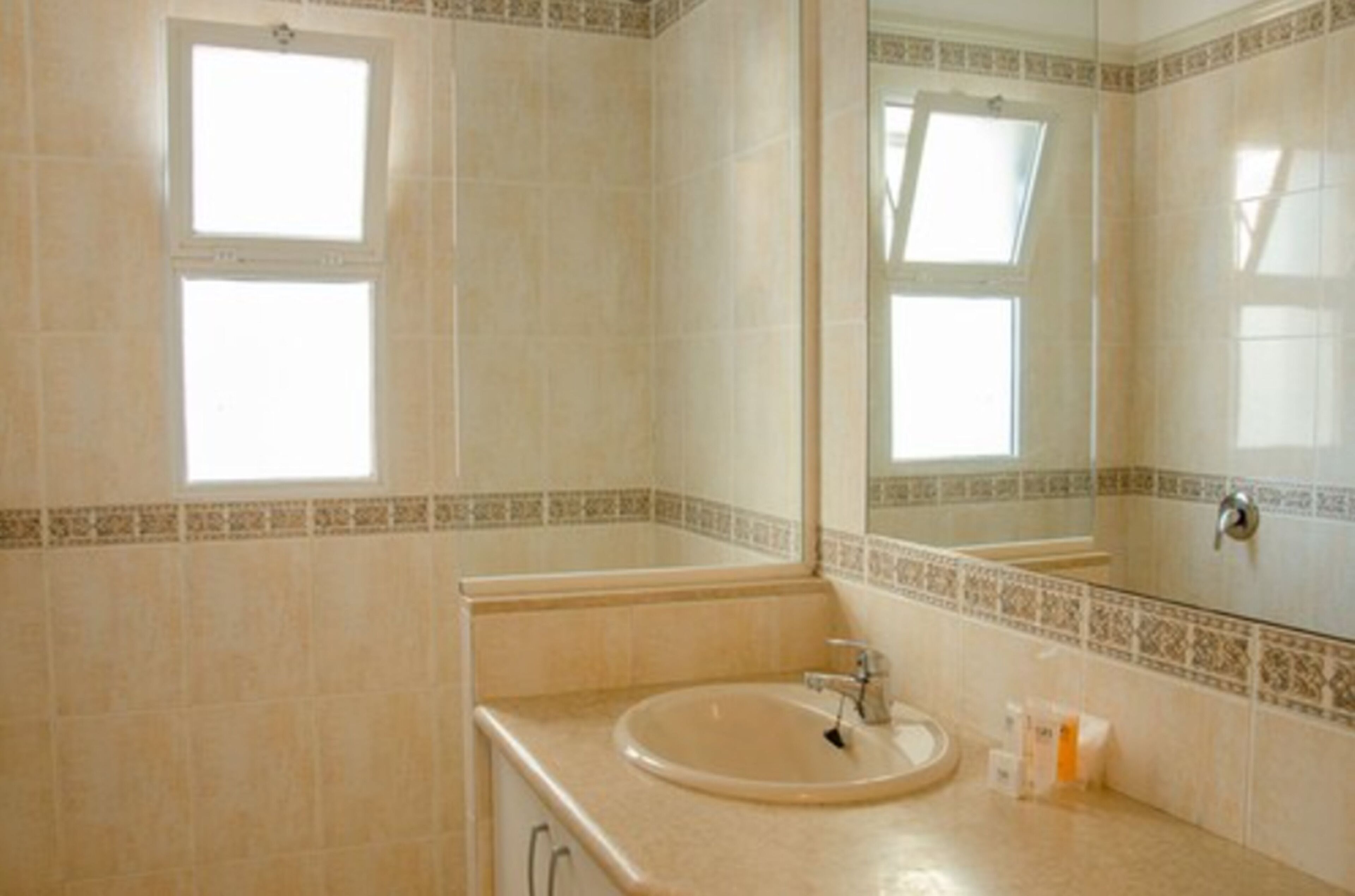 Un baño con lavamanos, espejo y dos ventanas.