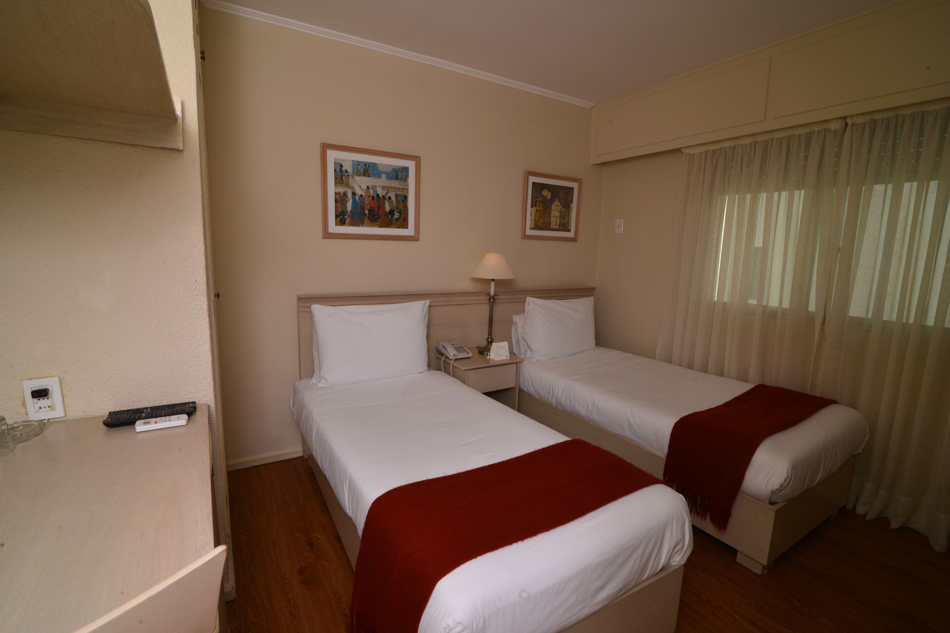 A hotel room with two beds, a nightstand with a lamp, and two framed pictures on the wall.