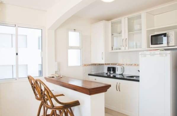 A modern kitchen with white cabinetry, a wooden island with bar stools, a microwave, and a coffee maker. - Sunset Beach Hotel (Punta del Este)