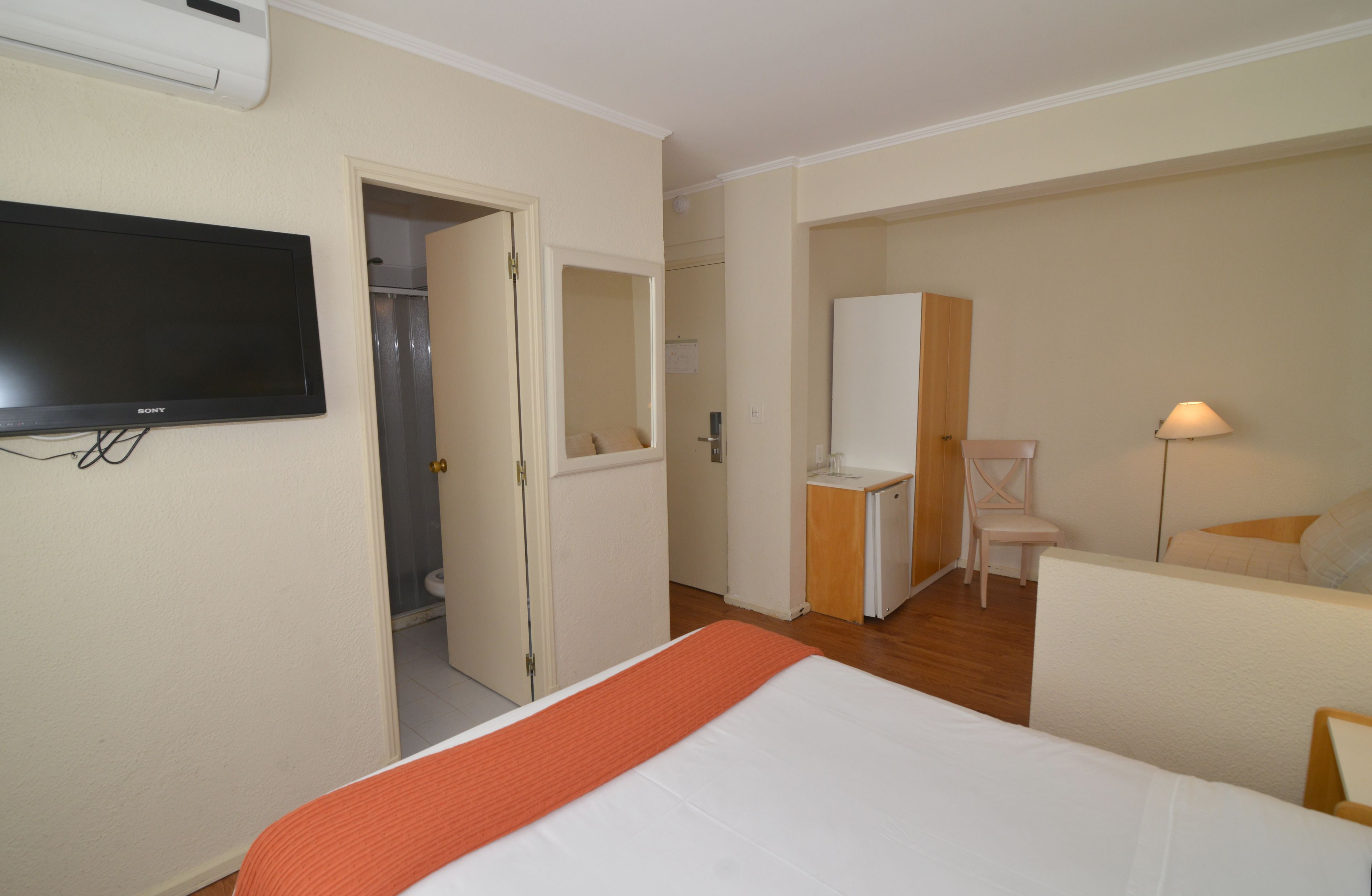 A hotel room with a bed, a TV, a desk, a chair, and a mirror.