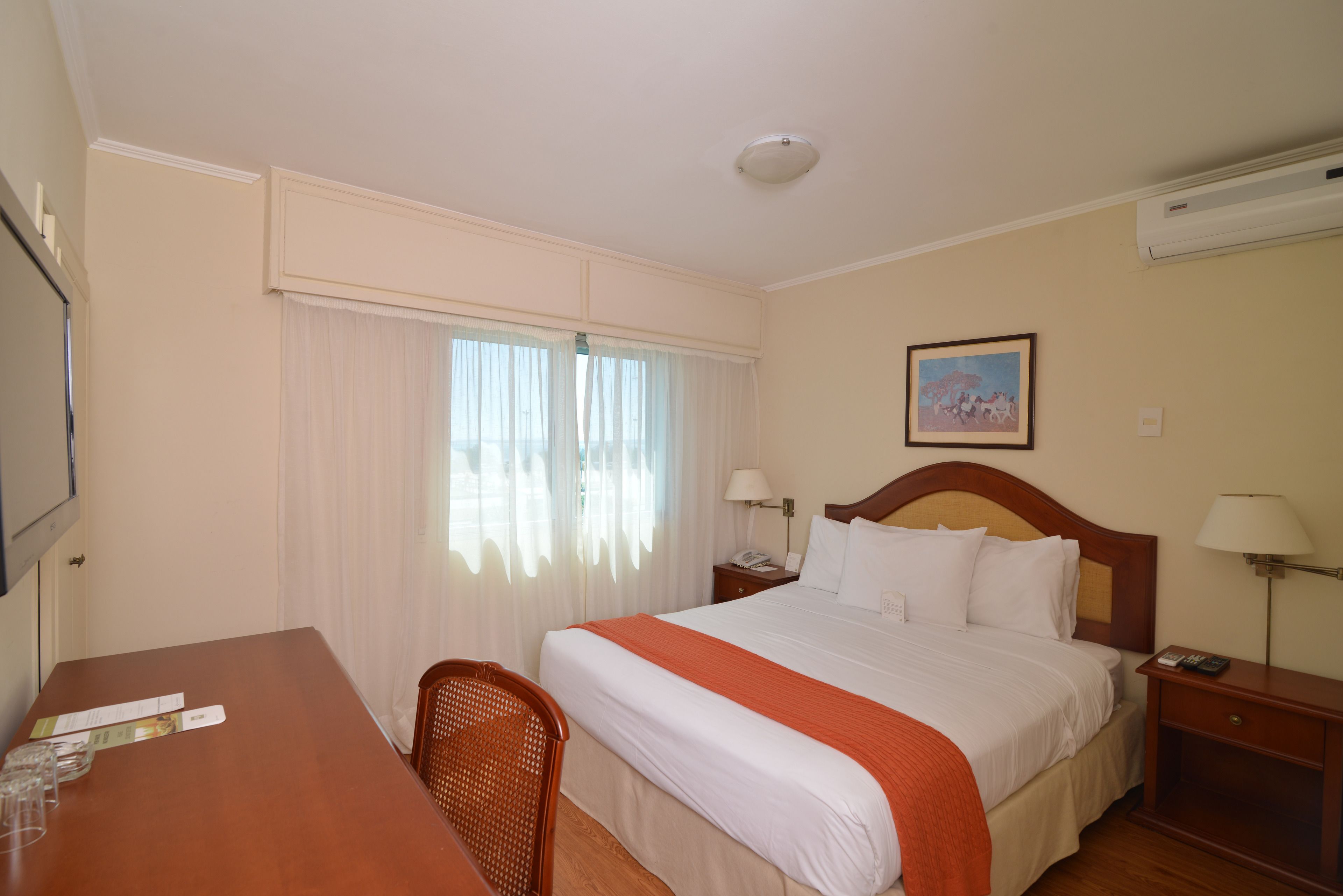 A hotel room with a bed, bedside tables, a desk, and a chair.