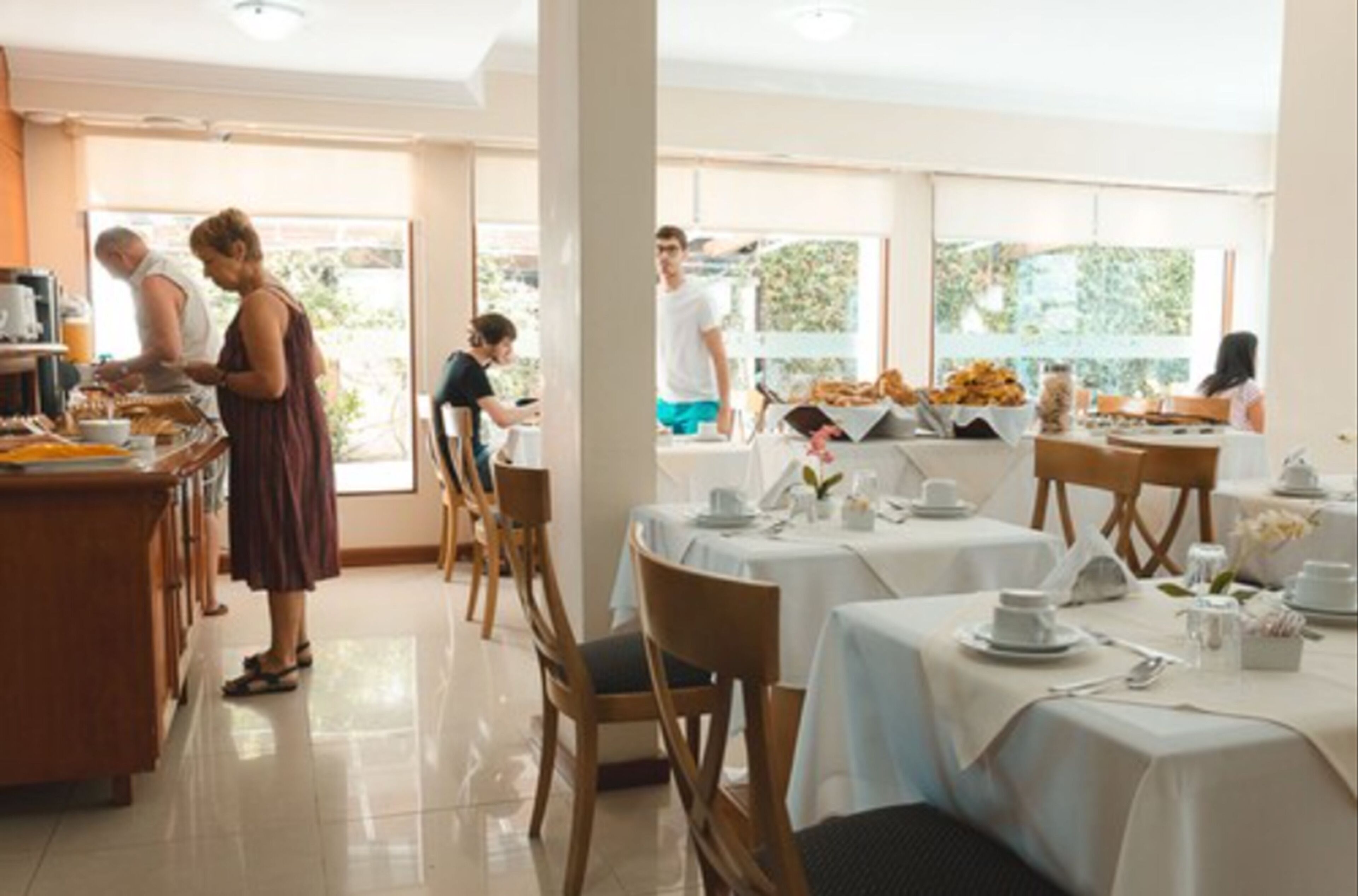 Un espace repas avec des tables dressées pour le service, un buffet et une vue sur l’extérieur.