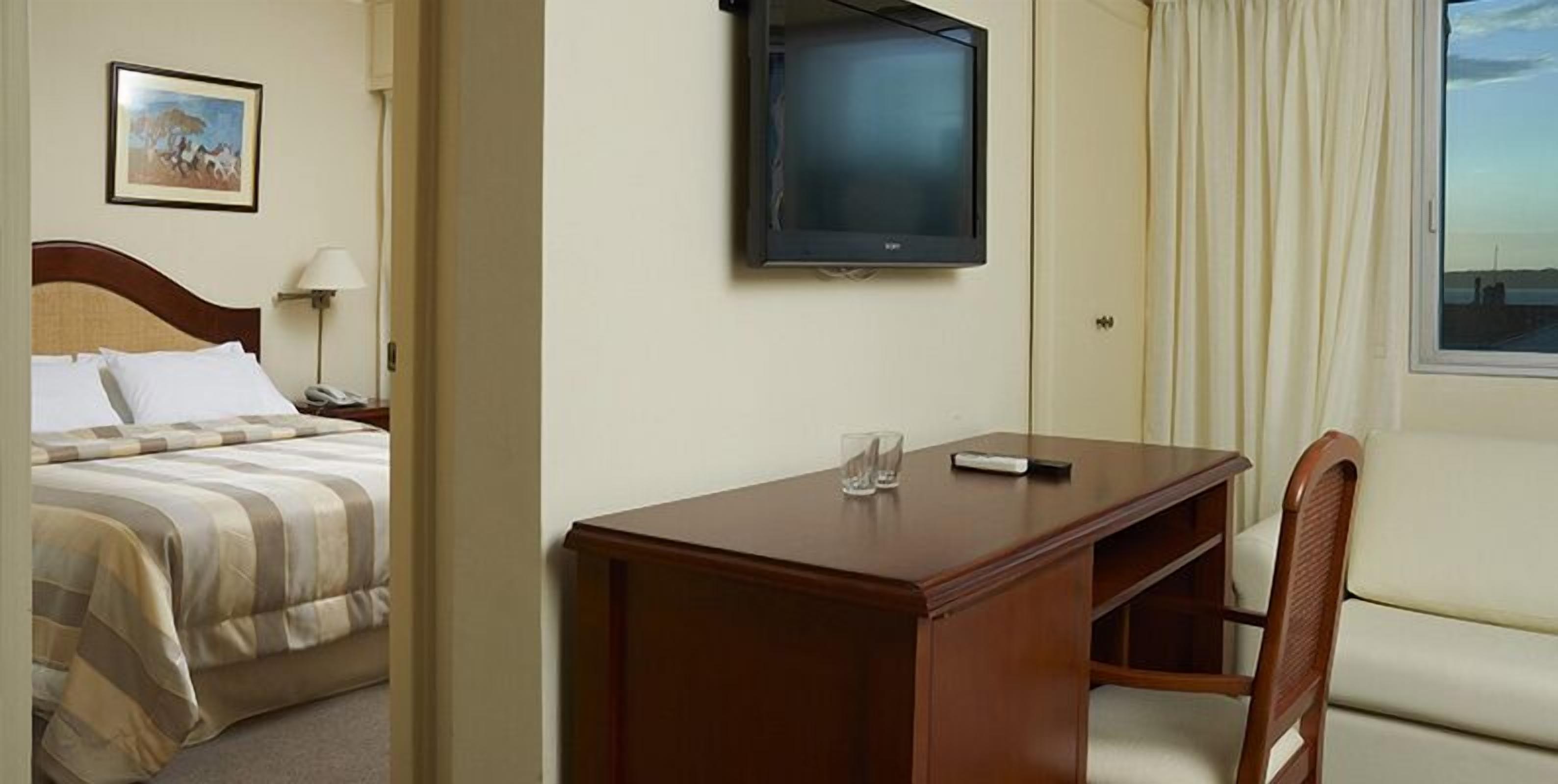 A hotel room with a bed, a desk, a chair, a television, and a window with curtains.