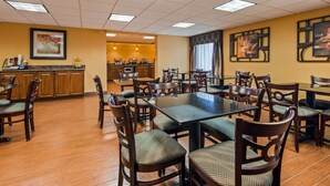Un comedor con varias mesas y sillas, una cocina al fondo y obras de arte en las paredes.