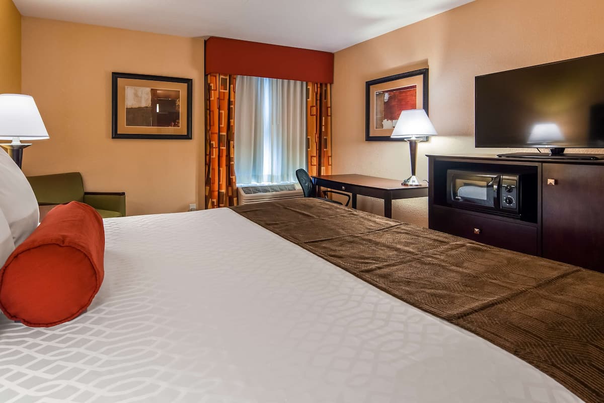 Une chambre d’hôtel avec un grand lit, un bureau, une télévision et une fenêtre avec des rideaux.