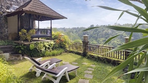 A gazebo with a stone wall, a stone staircase, and a view of a lush forest. There are two white lounge chairs with brown cushions. - Rijasa Agung Resort Villas (Ubud)