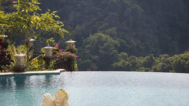A pool with a statue in the foreground, surrounded by lush greenery and a mountainous backdrop. - Rijasa Agung Resort Villas (Ubud)