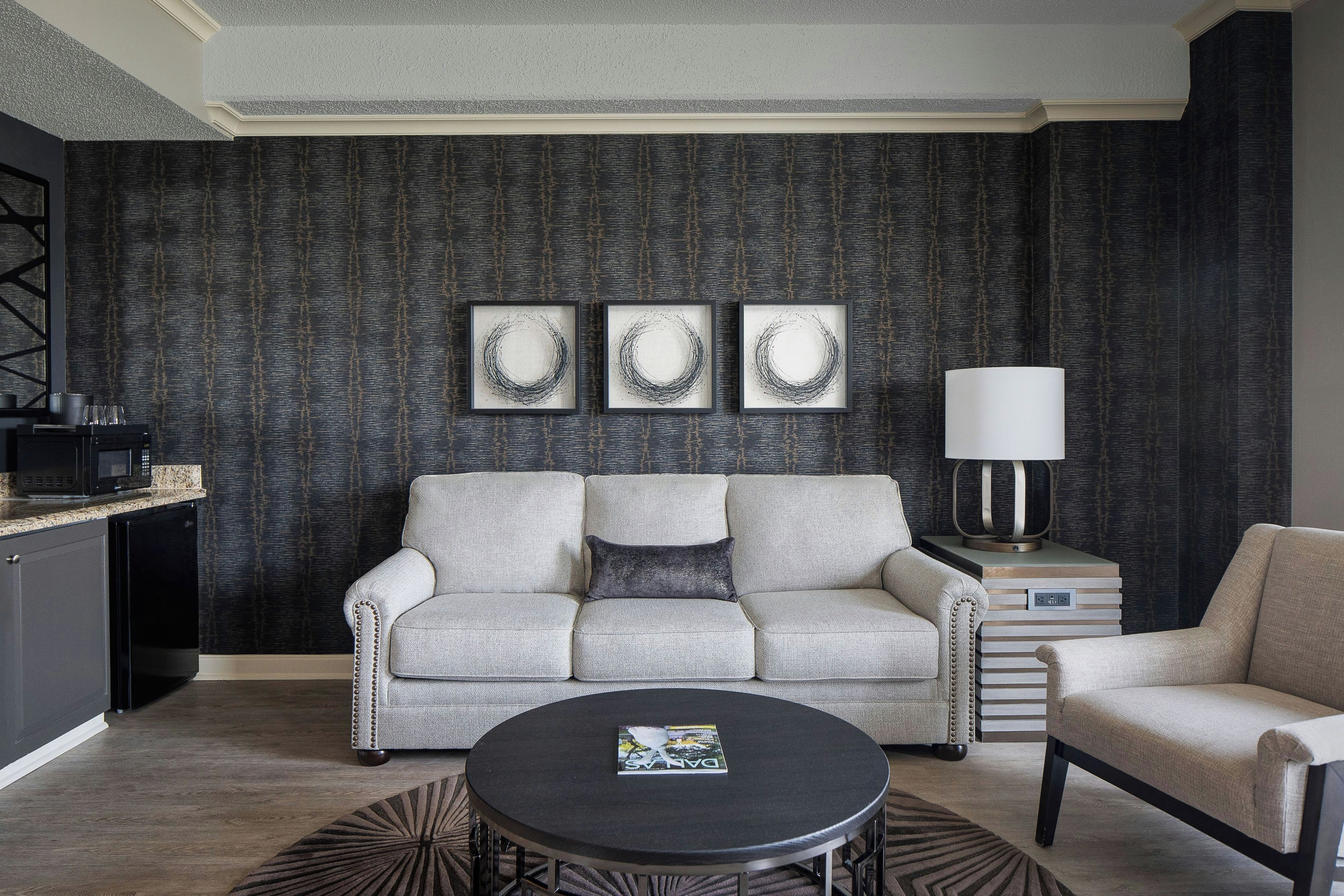 Uma sala de estar moderna com sofá, poltrona, mesa de centro e uma obra de arte na parede.