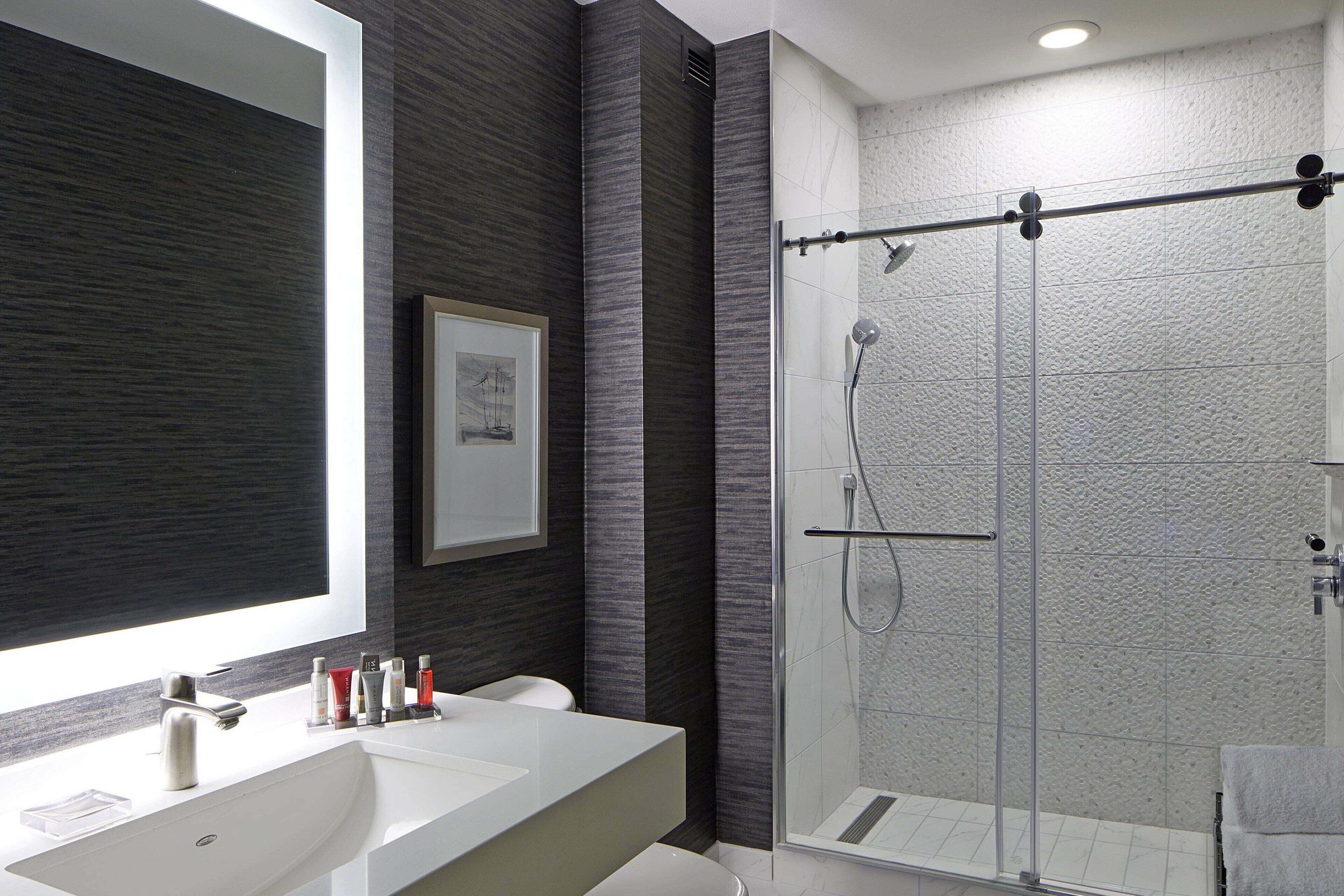 Une salle de bain moderne avec un grand miroir, un lavabo blanc et une cabine de douche en verre.