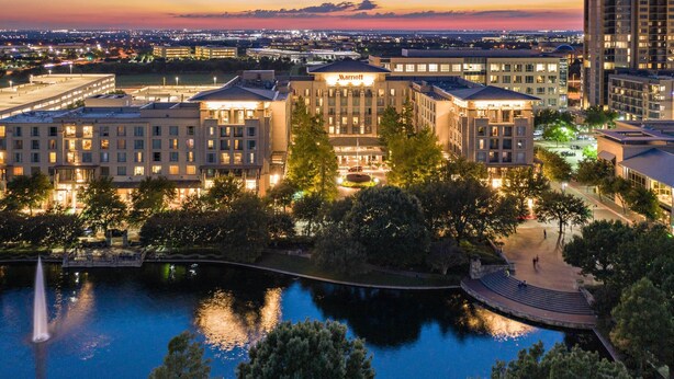 A Marriott hotel with a landscaped courtyard, a fountain, and a view of the surrounding cityscape at dusk. - Dallas/Plano Marriott at Legacy Town Center (Plano)