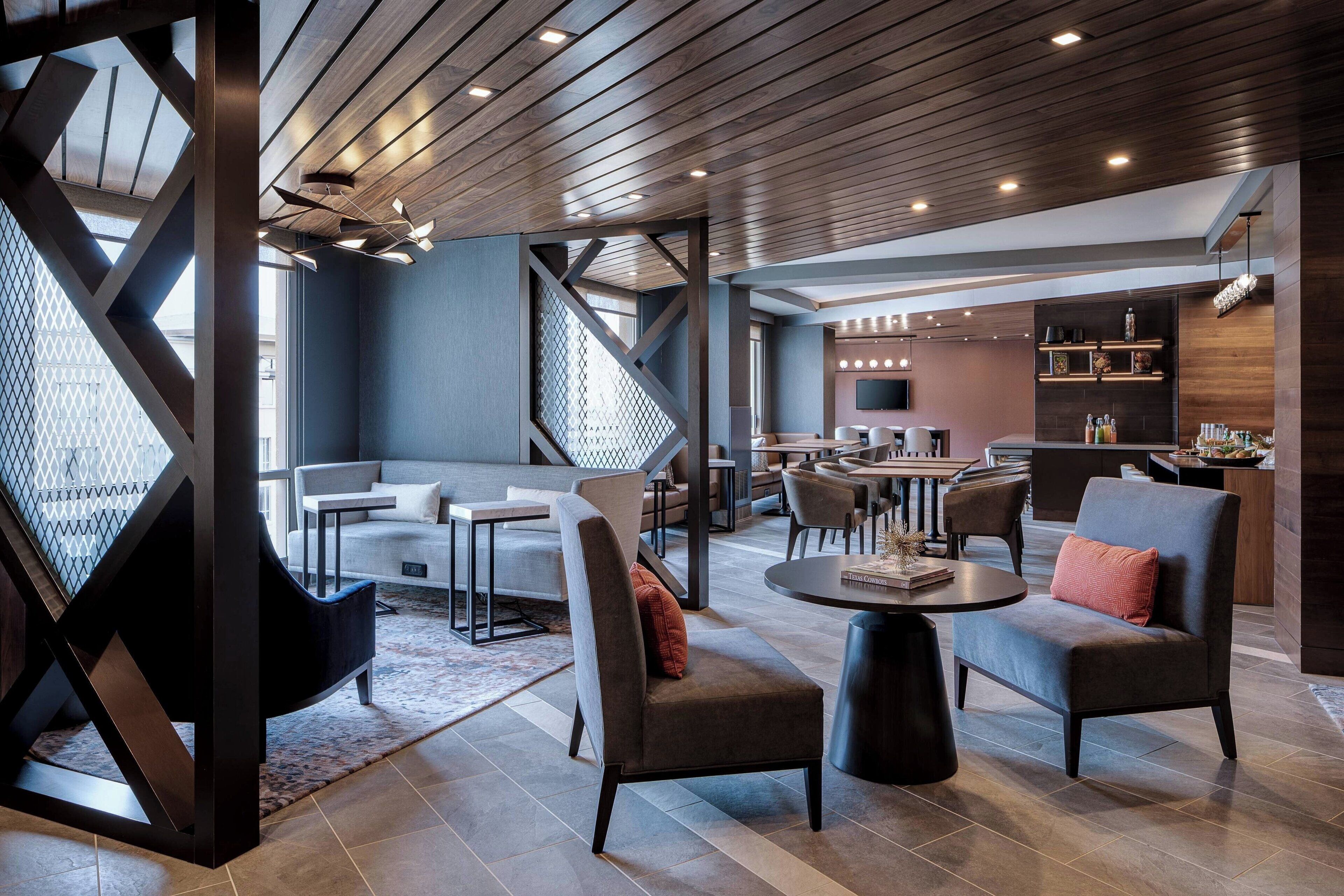 Un moderno espacio de salón con sofá, sillas, una mesa de centro y una zona de bar con estantes y televisor.