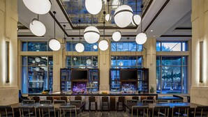A bar area with multiple seating options, a bar counter with a variety of bottles, and large windows providing views of the outside. - Dallas/Plano Marriott at Legacy Town Center (Plano)