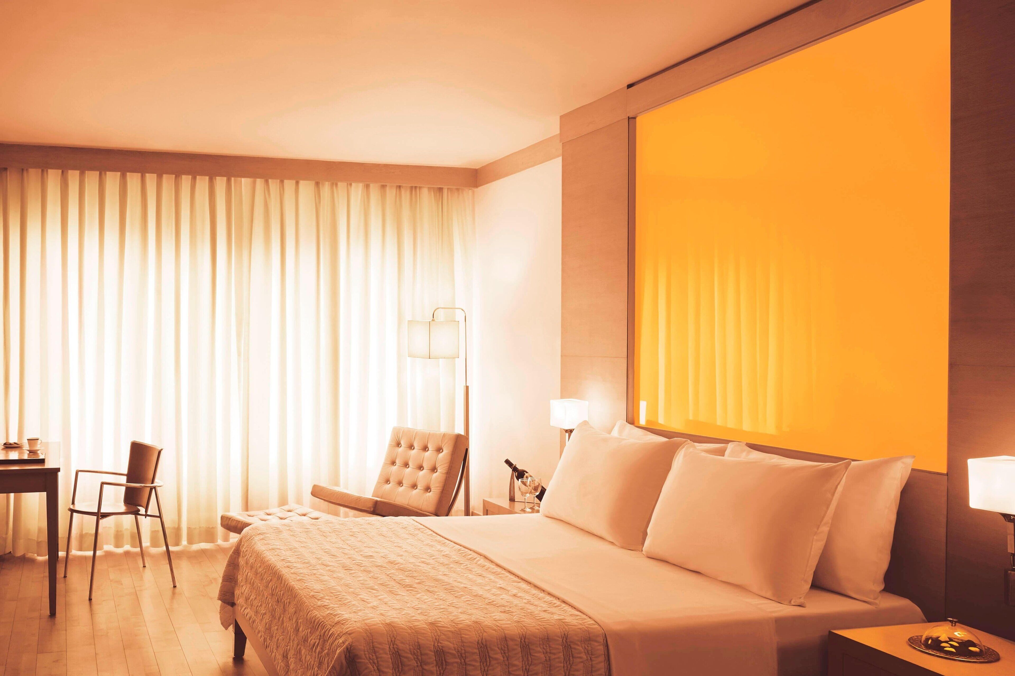 Hotelkamer met een groot bed, een bureau, een stoel en een nachtkastje met een lamp.